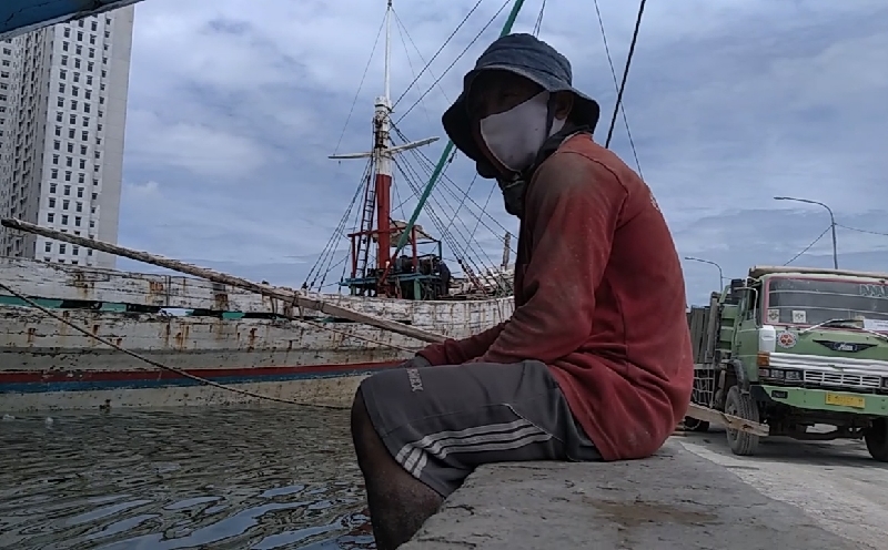 Seorang pekerja bongkar muat pelabuhan tengah beristirahat di pinggir dermaga. (Dok Reuters)